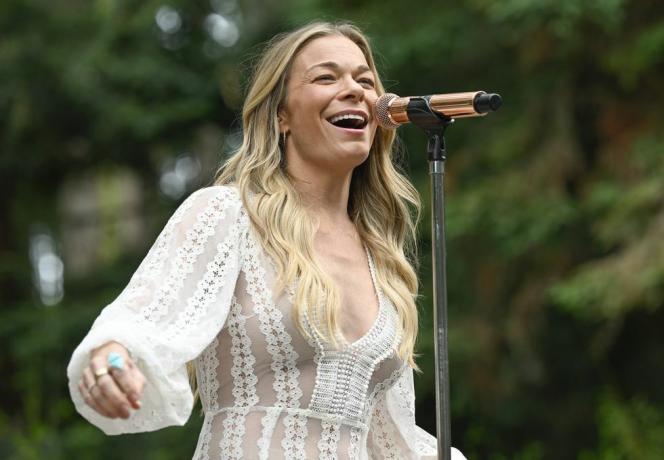 Η Leann Rimes τραγουδά στη σκηνή με μικρόφωνο σε λευκό δαντελένιο φόρεμα