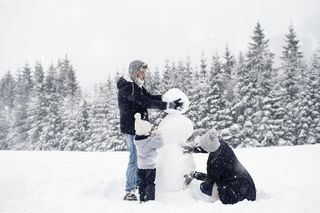 τριμελής οικογένεια χτίζοντας έναν χιονάνθρωπο στο χιόνι