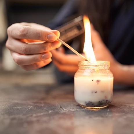 καλλιεργήστε ανώνυμη γυναίκα με αναμμένο σπίρτο που ανάβει αρωματικό κερί σε γυάλινο βάζο τοποθετημένο σε μαρμάρινο τραπέζι στο σπίτι