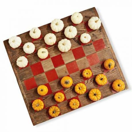μια ξύλινη σανίδα ζωγραφισμένη σαν ένα παιχνίδι πούλι χρησιμοποιώντας μίνι κολοκύθες σε λευκό και πορτοκαλί ως κομμάτια του παιχνιδιού