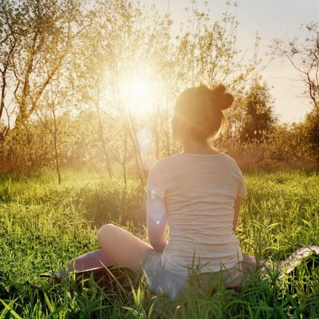νεαρή γυναίκα που κάθεται σε θέση γιόγκα απολαμβάνοντας το ηλιοβασίλεμα στη φύση