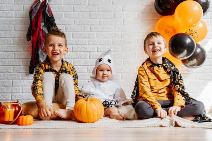 τα παιδιά με κοστούμια γιορτάζουν το Halloween λευκό τοίχο από τούβλα με διακοσμητικά αντίγραφο χώρου